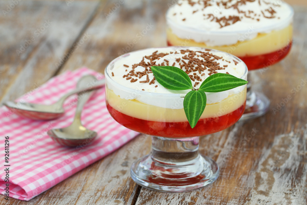 Traditional English strawberry trifle in transparent dessert glass on rustic wooden surface