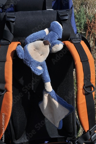 Une peluche de bébé posée sur un sac à dos de randonneur  lors d'une pause photo