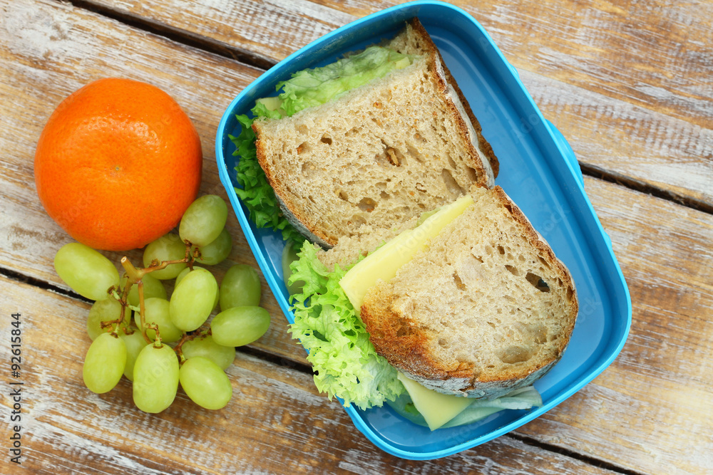 Healthy lunch box containing rustic bread sandwiches with cheese and lettuce, grapes and mandarine
Healthy lunch box containing rustic bread sandwiches with cheese and lettuce, grapes and mandarine