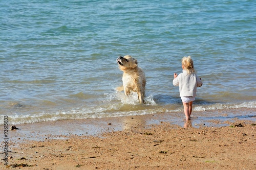 Une jeune enfant marche dans l'eau avec son beau chien sur une plage de sable