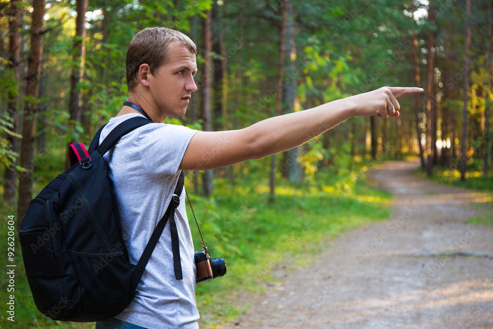 young man with backpack showing on something in forest young man with backpack showing on something in forest