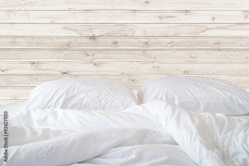 Foto White bedding sheets and pillow on wooden wall room background,