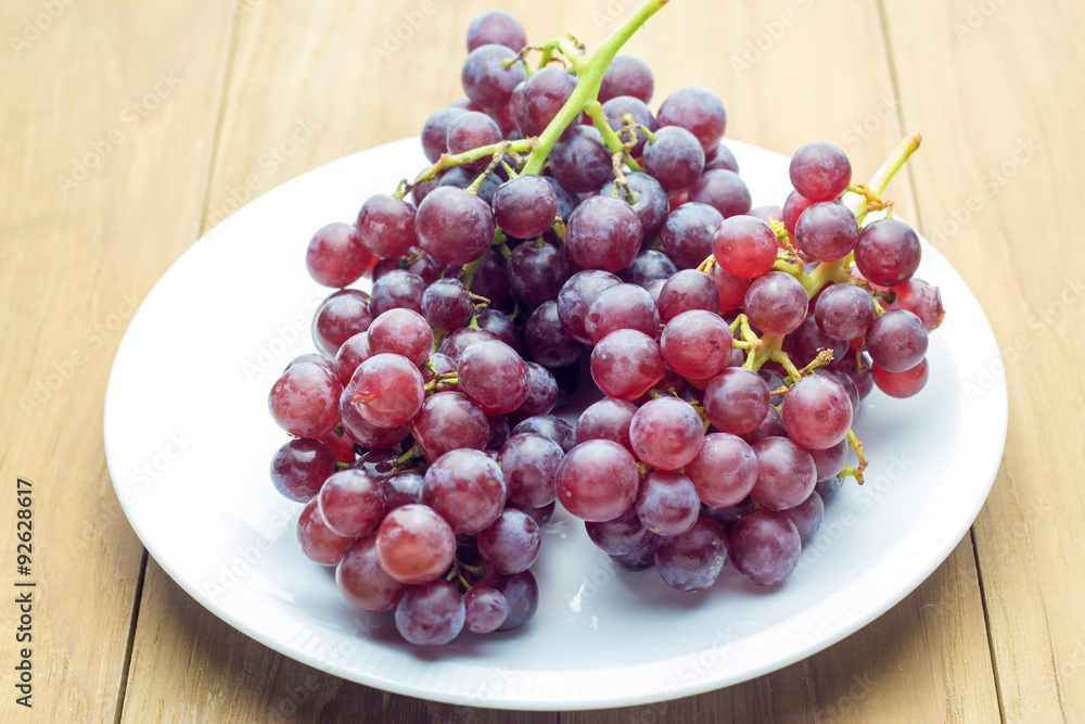 red bunch grape in white dish on wooden board red bunch grape in white dish on wooden board