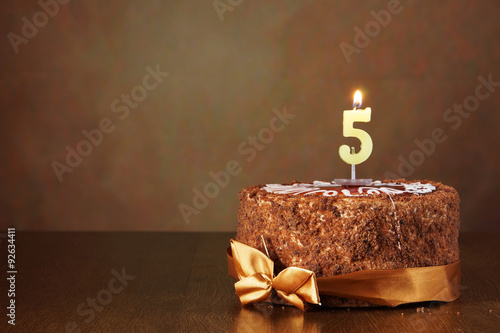 Birthday chocolate cake with burning candle as a number five on brown background