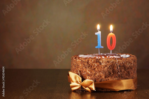 Birthday chocolate cake with burning candle as a number ten on brown background