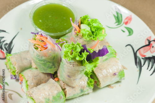 Portion of spring rolls on old wood with spicy sauce, vegetables