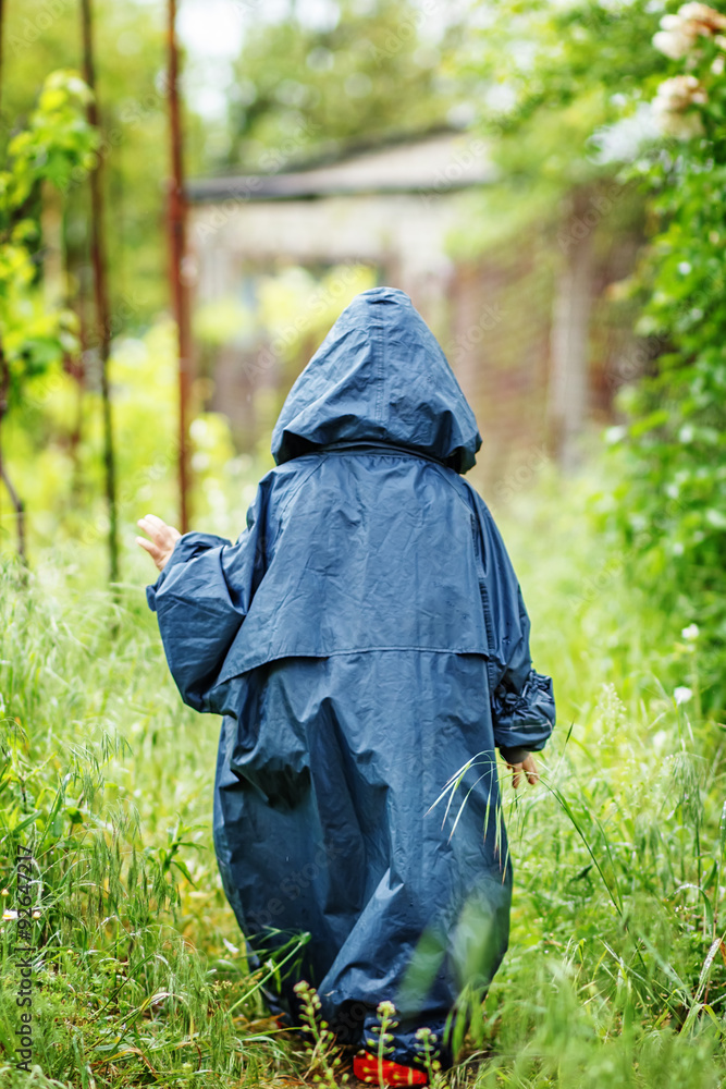 Funny little boy walks in the rain in a raincoat with a hood. Funny little boy walks in the rain in a raincoat with a hood.