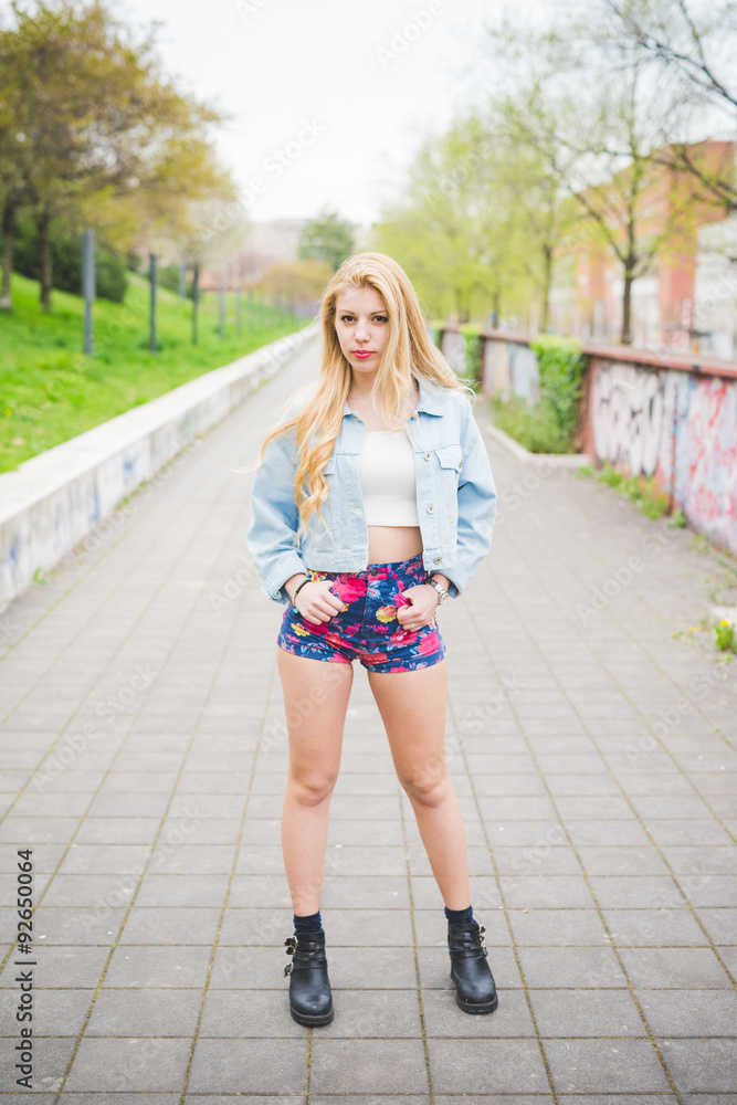 Young handsome blonde caucasian fashion girl posing on a park in