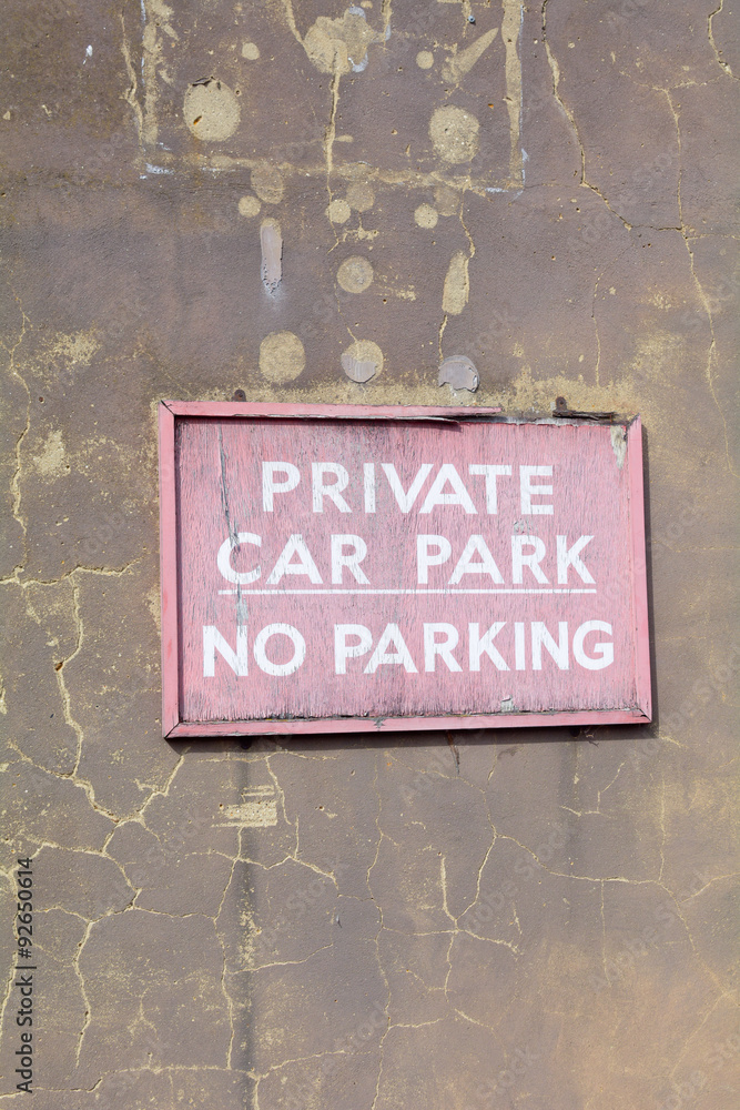 Fototapeta premium Faded and cracked wooden 'Private Car Park - No Parking' sign on wall