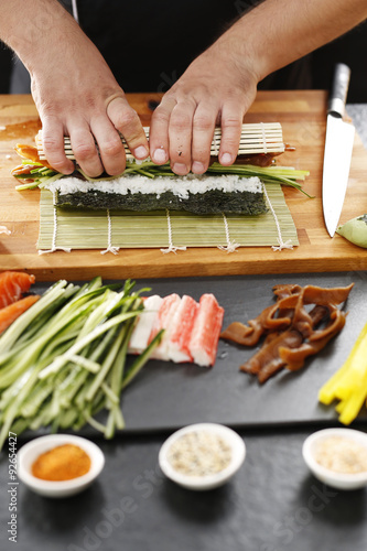 Sushi , etapy przygotowywania sushi z łososiem, paluszkiem krabowym, ogórkiem tykwą zawiniętego w glon nori