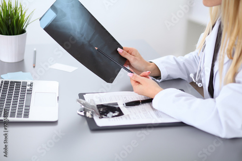 Close up of female doctor holding x-ray or roentgen image, sitting at the table
