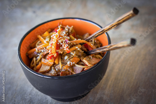 Fotografie Stir fry with vegetables and meat garnished with sesame seeds in bowl with chopsticks
