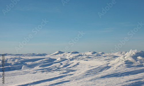 Snow desert and blue winter sky. Mountains on the horizon