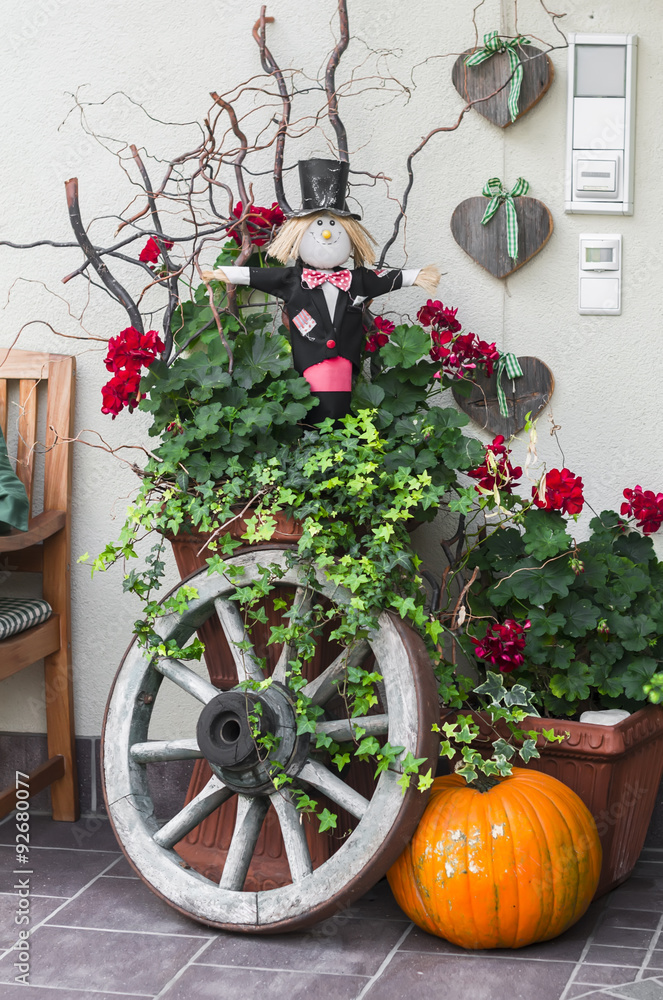 Halloween decoration - pumpkin, Scarecrow, old wooden wheel near the door of the house