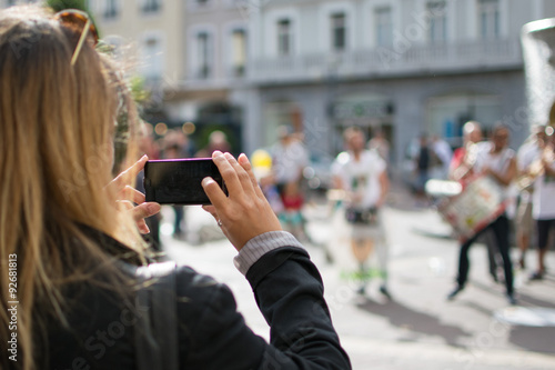 Une femme filme avec son téléphone portable un orchestre en train de jouer sur la place Grenette à Grenoble