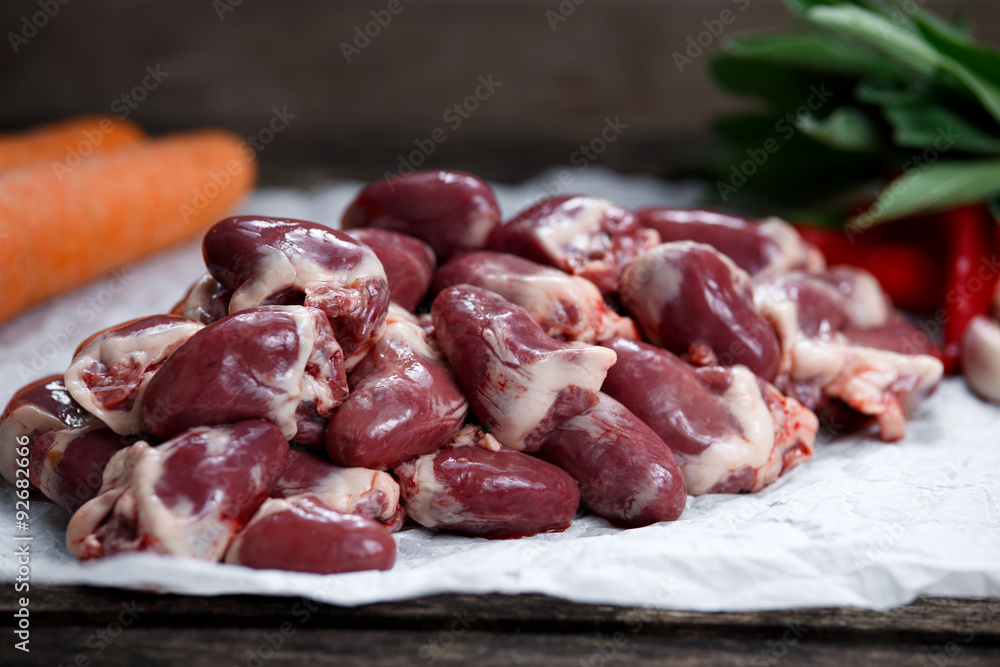 Raw Duck hearts on crumpled paper, decorated with vegetables. on old wooden table Raw Duck hearts on crumpled paper, decorated with vegetables. on old wooden table
