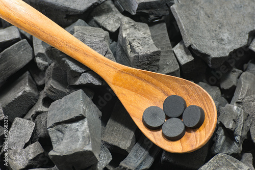 activated carbon pill in wood spoon on charcoal texture background