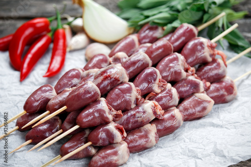 Ready to cook Duck Heart stringed on skewers BBQ , chili pepper. decorated with greens and vegetables. background