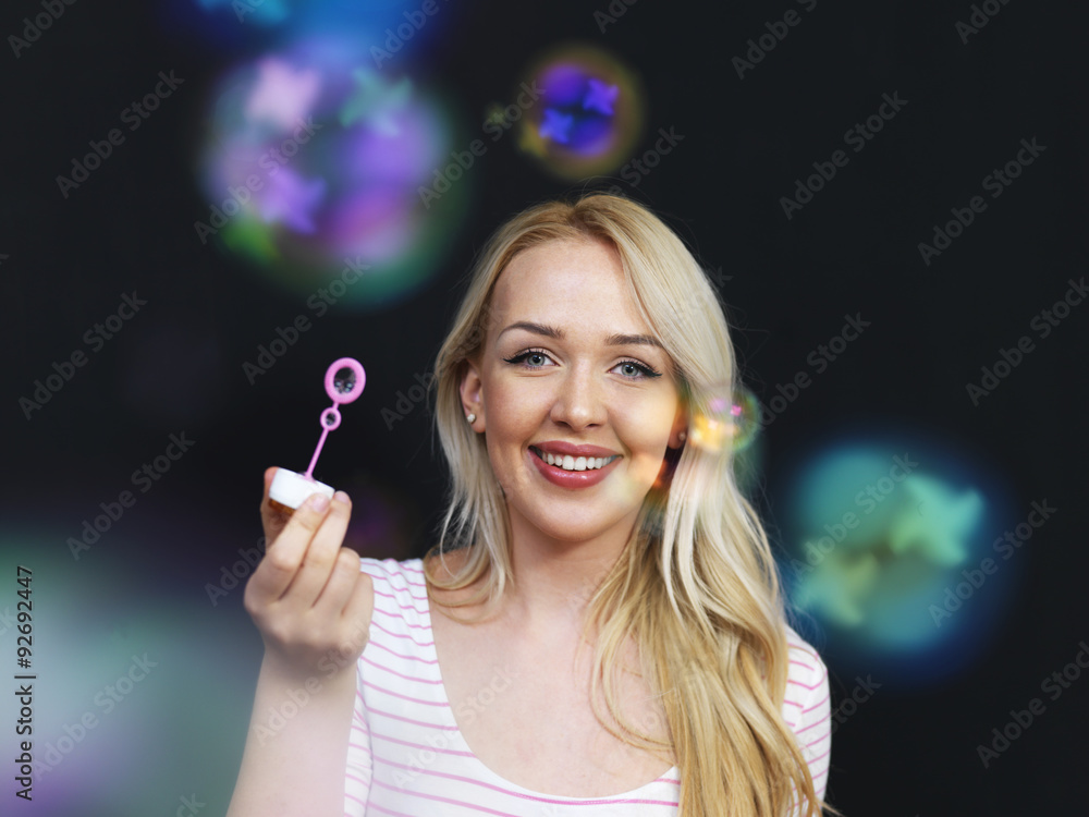 Obraz premium Woman blowing bubbles on black background as she celebrate speci