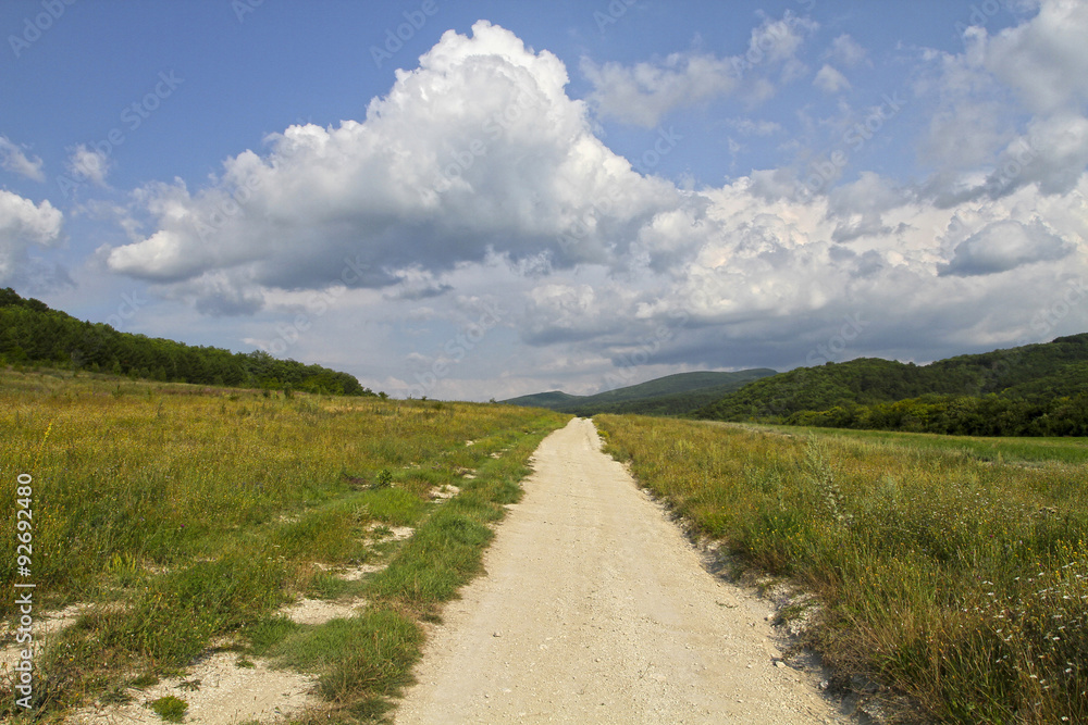 Unpaved dirt road takes to the sky with clouds