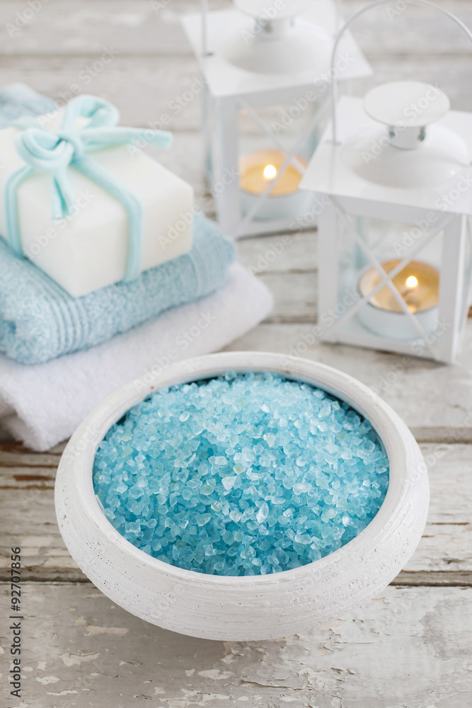 Bowl of blue sea salt, two towels and bar of handmade soap on wooden table