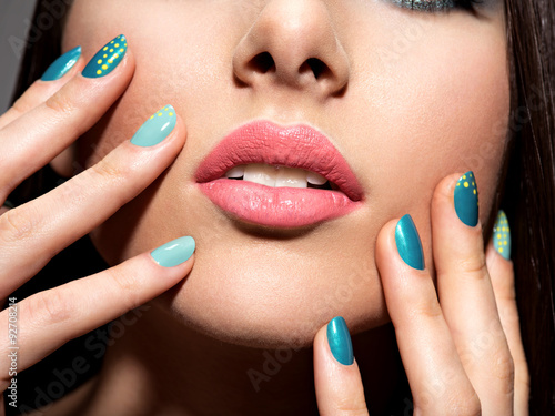 Woman's fingers with motton blue color of the nails on the face