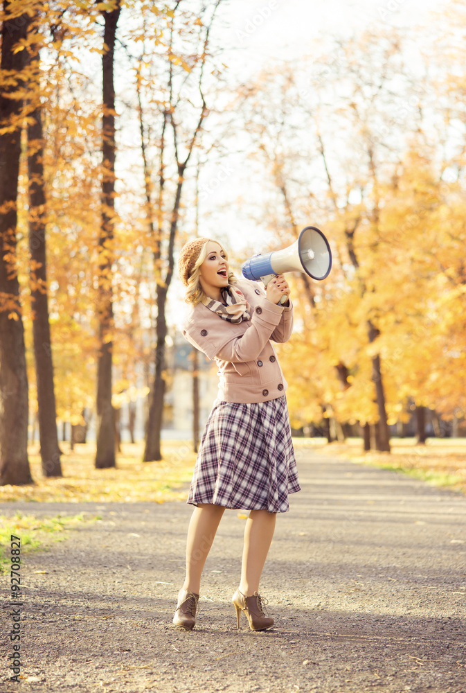 Attractive young woman yelling with loudspeaker in the autumn park.
