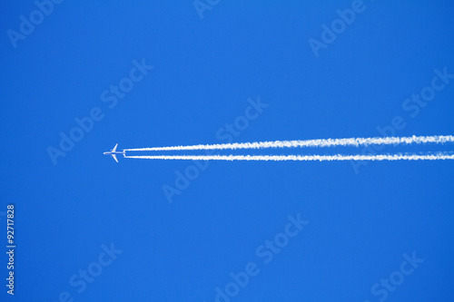 Airplane with condensation trails on blue sky.