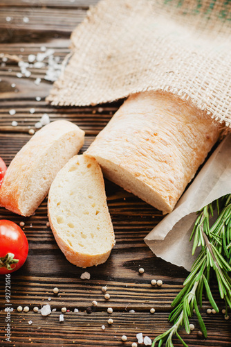 
Italian ciabatta with tomatoes , salt, pepper and rosemary on the wooden background