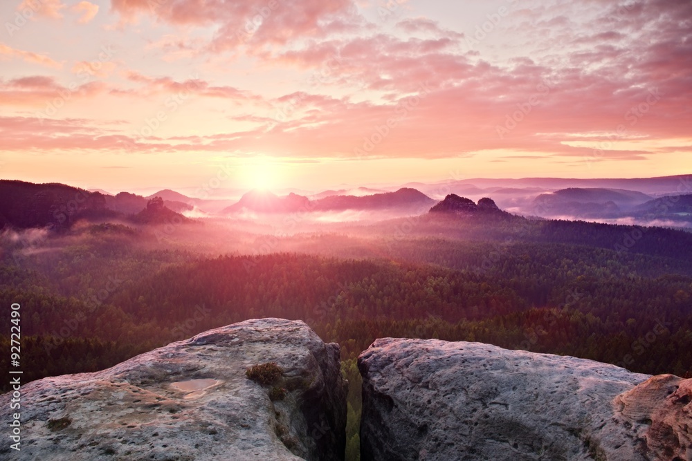 View over sandstone cliff into deep misty valley in Saxony Switzerland. Sandstone peaks increased from heavy foggy background.