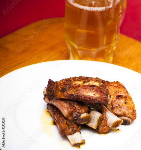 Roasted pork ribs on a white plate with a pitcher of beer next