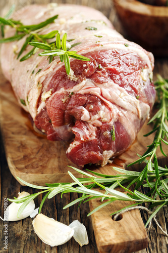 Raw boneless lamb leg with garlic and rosemary on wooden backgro