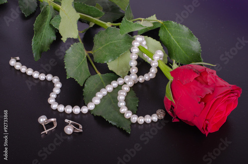 Fototapeta Naklejka Na Ścianę i Meble -  Red rose, pearls earrings and necklace on a black background