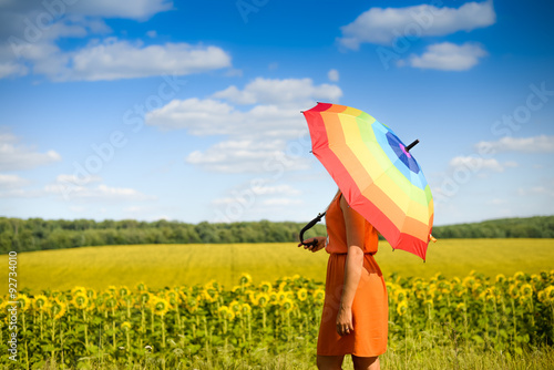 Female under umbrella standing in field of sunflowers