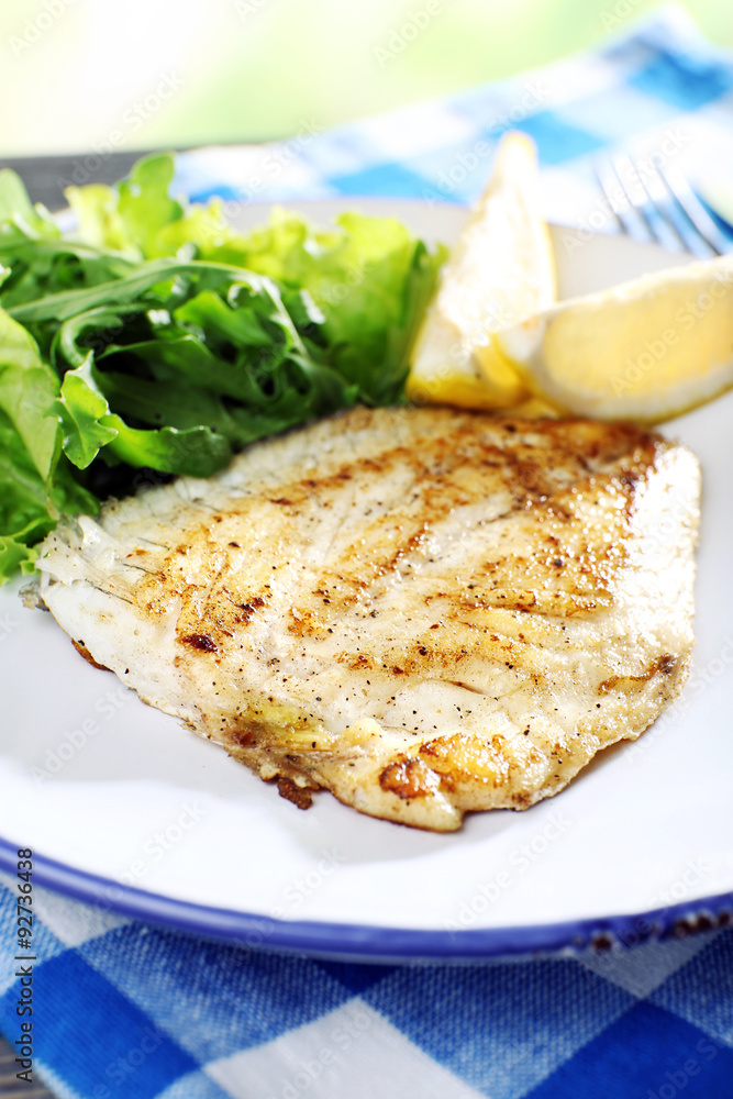 Dish of fish fillet with lettuce and lemon on table close up Dish of fish fillet with lettuce and lemon on table close up