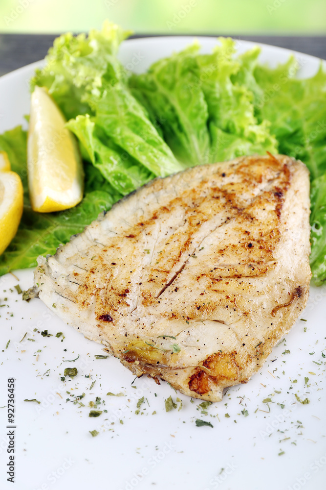 Dish of fish fillet with greens and lemon on plate close up Dish of fish fillet with greens and lemon on plate close up