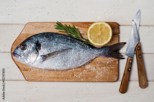 Salted dorada, rosmarine, lemon, board and knifes photo