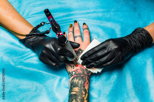 Fotografie Tattooist draws orange paint on clients tattoo