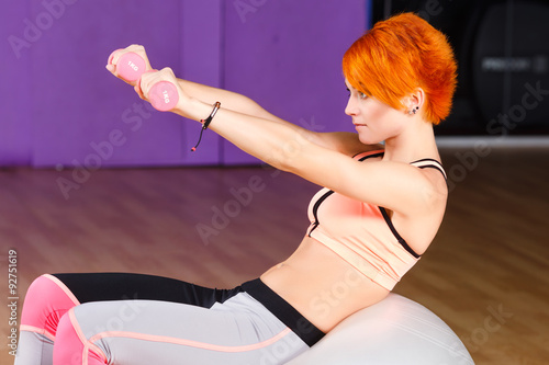 Attractive young girl does exercises with dumbbells in the gym
