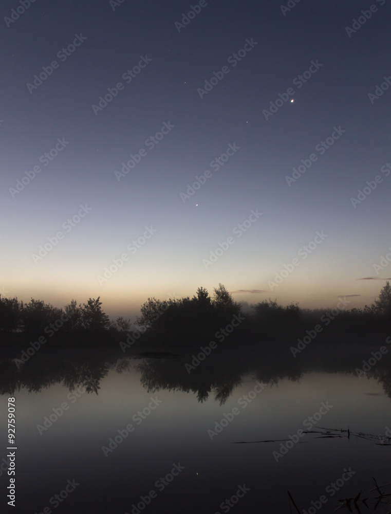 Riverside just before sunrise.
Trees reflected in the water. Stars in the sky.