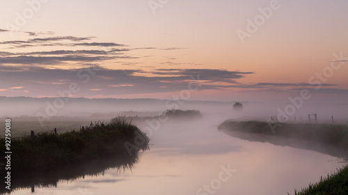 River in the fog, just before sunrise. Warm glow in the clouds from the first sunrays.
