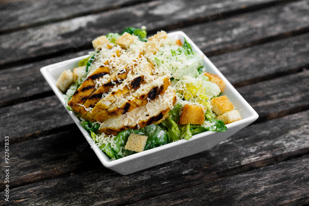 Caesar salad with chicken and lettuce on wooden table Caesar salad with chicken and lettuce on wooden table