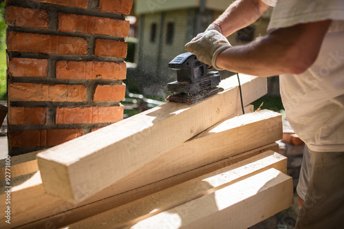 Foto Senior man finishing wooden beam with sander