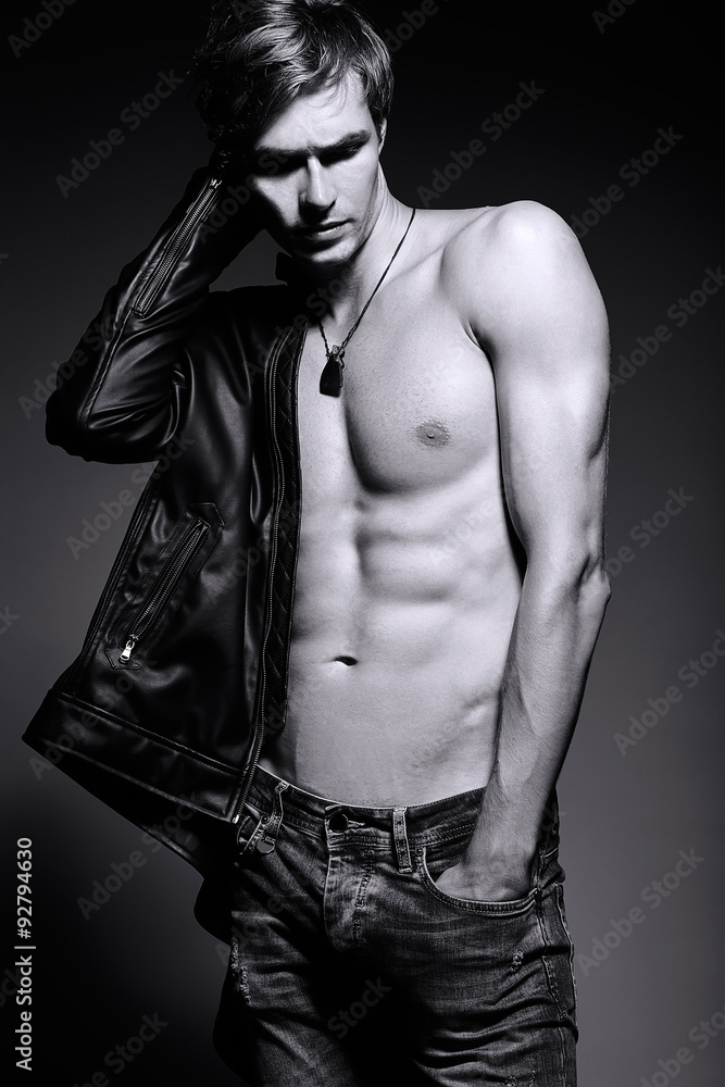 Naklejka premium Young handsome muscled fit male model man in leather jacket posing in studio showing his abdominal muscles