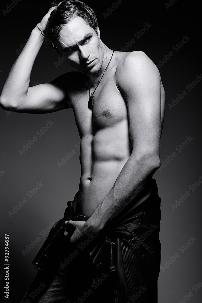 Obraz premium Young handsome muscled fit male model man in leather jacket posing in studio showing his abdominal muscles