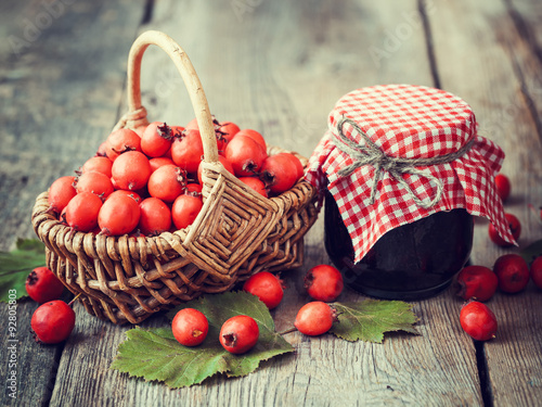 Jar of jam and hawthorn berries in basket on rustic table photo