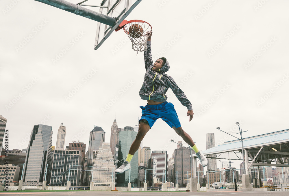 Fototapeta premium basketball player performing slum dunk on a street court. background with manhattan buildings