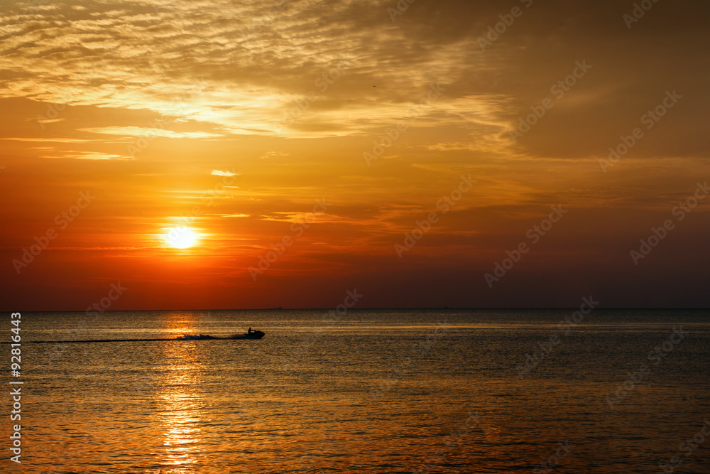 Silhouette of a man on a jet ski in the sea at sunset.