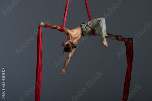 Sporty young man doing exercise with elastics, aerial silk ribbons, aerial. Sport training gym and lifestyle concept. Anti-gravity yoga.