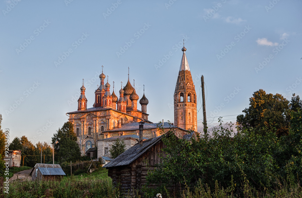 Evening rural landscape with old church and wooden houses